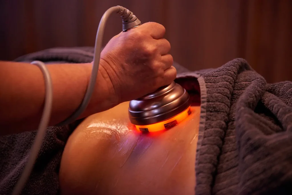Närbild på ett handstycke med orange ljus som förs över huden under en cavitationsbehandling.