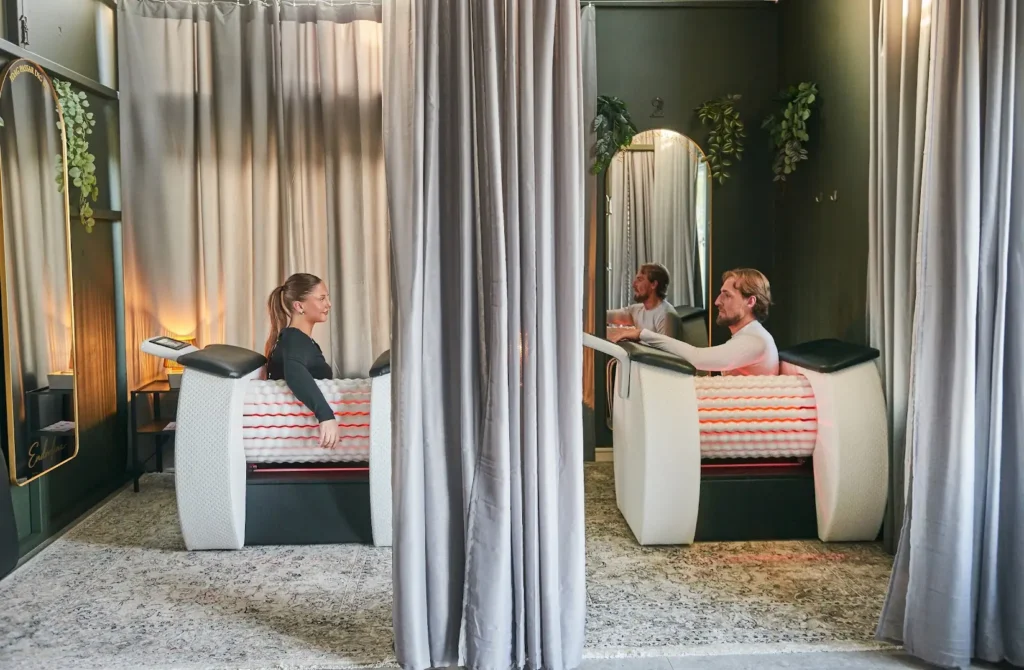 Två personer i varsin rollmassagemaskin med rött ljus, i ett rum med grå draperier och mjuk belysning hos Endorfina.